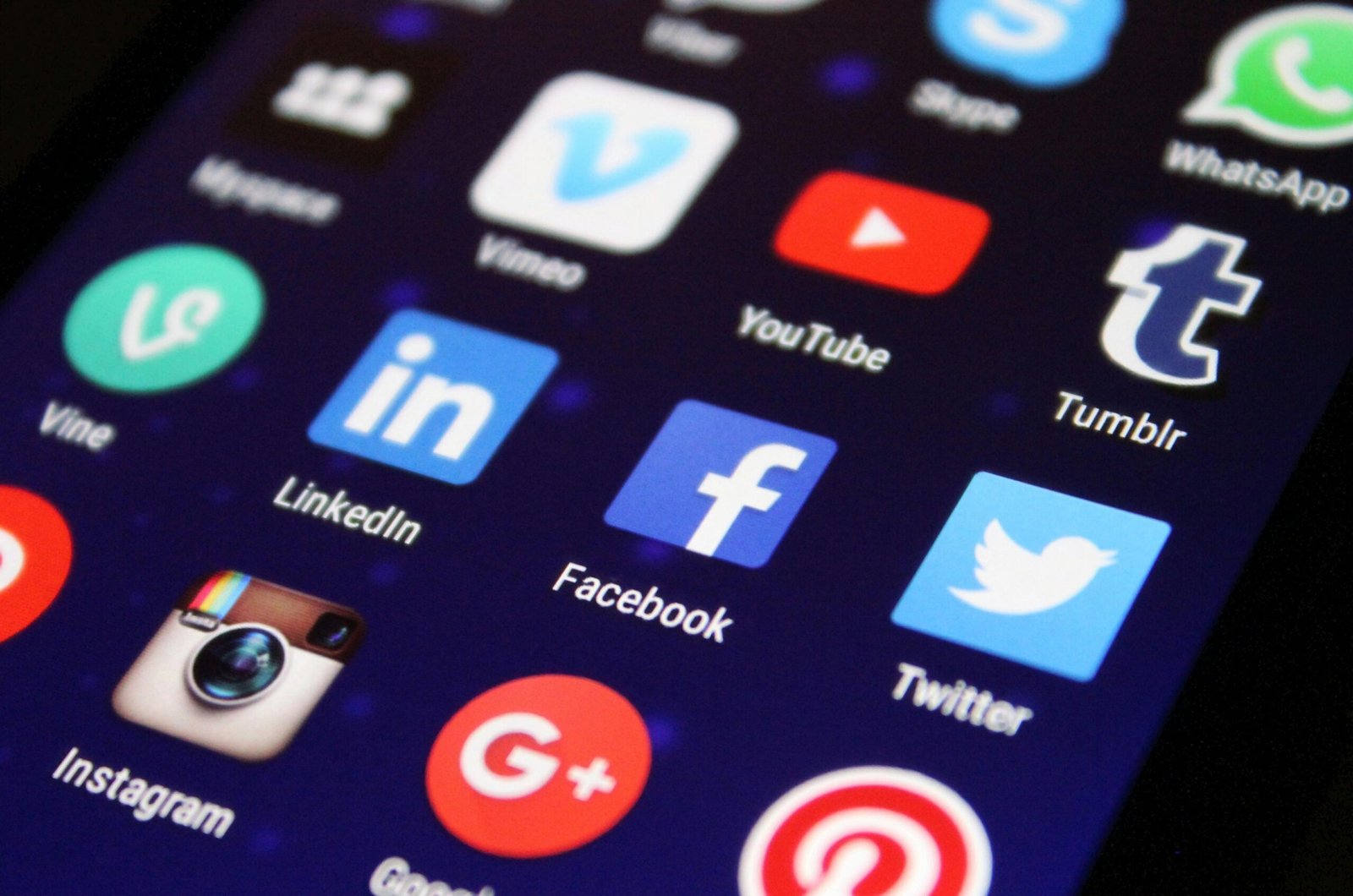 Close-up of a smartphone screen displaying various social media app icons, including Facebook, Twitter, Instagram, LinkedIn, Pinterest, YouTube, and others, with a dark background